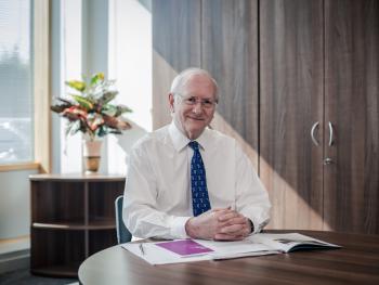 Dr Alan Billings smiling sitting at his desk