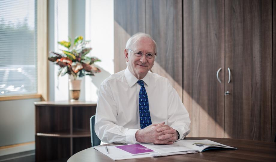Dr Alan Billings smiling sitting at his desk