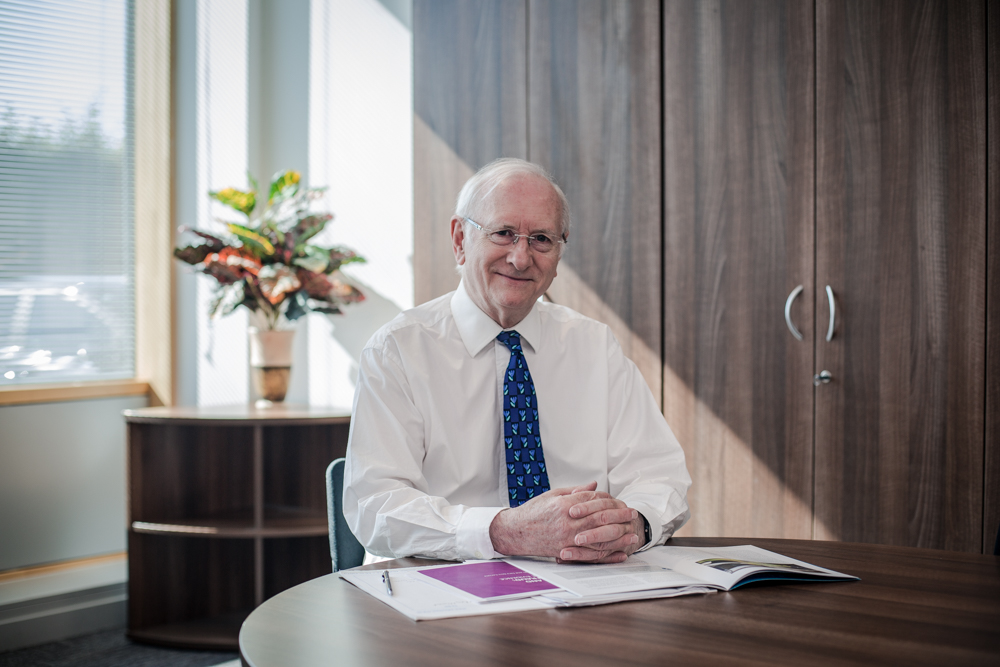 Dr Alan Billings smiling sitting at his desk